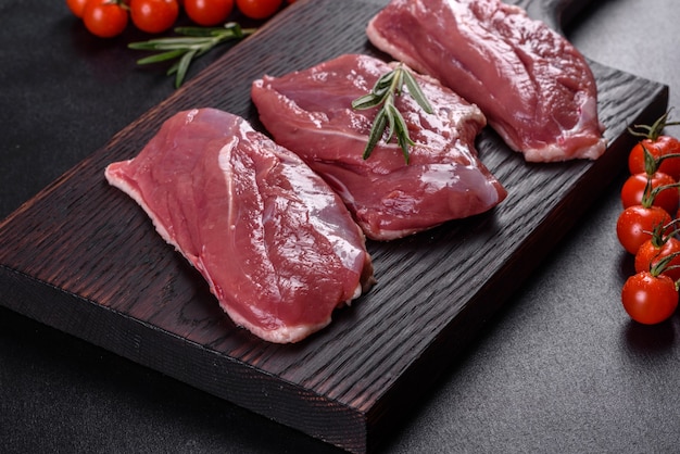 Rohe Entenbrust mit Kräutern und Gewürzen auf einem dunklen Tisch. Rohes Fleisch zum Backen vorbereitet