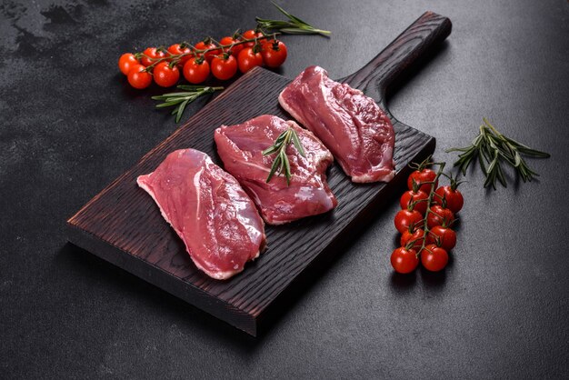 Rohe Entenbrust mit Kräutern und Gewürzen auf einem dunklen Tisch. Rohes Fleisch zum Backen vorbereitet