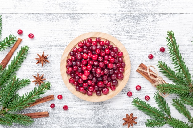 Rohe frische Cranberries in Holzschale, Gewürz- und Tannenzweigen auf hellem Holzhintergrund. Ansicht von oben - Bild