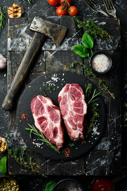 Rohe frische Schweinesteaks mit Gewürzen und Kräutern Draufsicht auf schwarzem Steinhintergrund