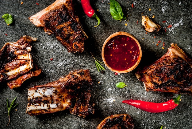 Rohe Frischfleisch-, gebratene oder gegrillte Lamm- oder Rindfleischrippen mit roter Tomatensauce, Peperoni, Knoblauch und Gewürzen auf dunklem Stein, Draufsicht copyspace