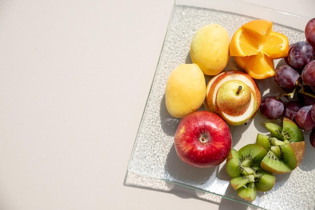 Rohe Früchte, Beeren, Orangen, Kiwi, Grapefruit, Trauben, Birnenäpfel auf dem Teller auf dem weißen Tisch