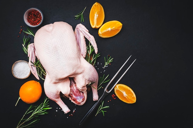 Rohe ganze Ente mit Orangenpfeffer und Rosmarin Bereit zum Backen für ein festliches Abendessen Schwarzer Tischhintergrund Draufsicht Kopierbereich