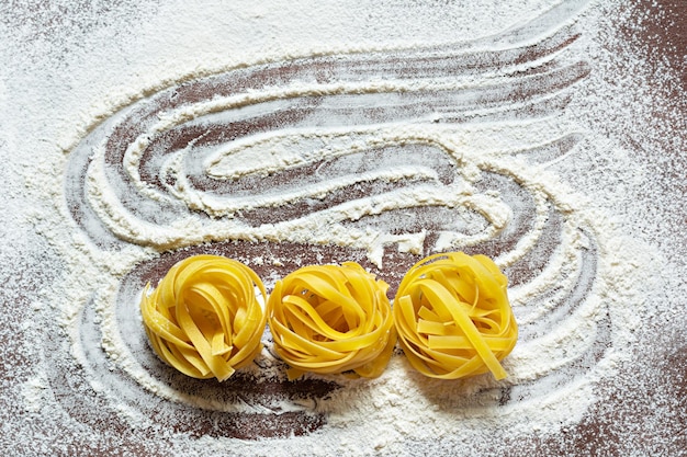 Rohe gelbe italienische Pasta (Nester) Pappardelle, Fettuccine oder Tagliatelle auf braunem Hintergrund