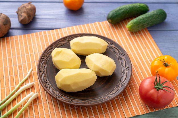 Rohe geschälte Kartoffelknollen auf einem Teller auf dem Küchentisch mit Gemüse. Vorbereitung zum Kochen.