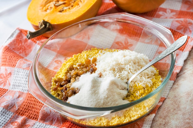 Rohe gewaschene Hirse, Reis und Rosinen in einer Glaswanne bei dem Kochen des Milchkürbisbreis