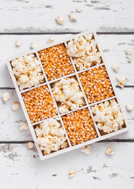 Rohe goldene Zuckermais-Samen und Popcorn in der weißen Holzkiste auf hellem Hintergrund