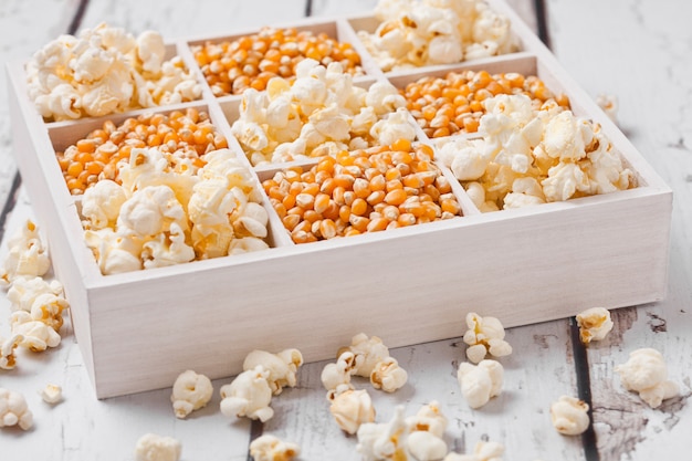 Rohe goldene Zuckermais-Samen und Popcorn in der weißen Holzkiste auf hellem Hintergrund