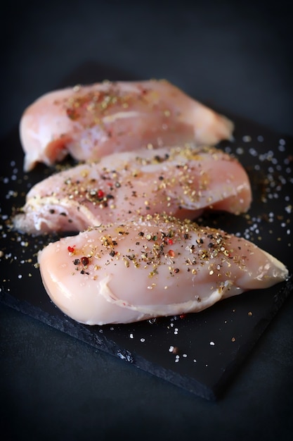 Foto rohe hähnchenfilets mit gewürzen auf einem steinbrett.