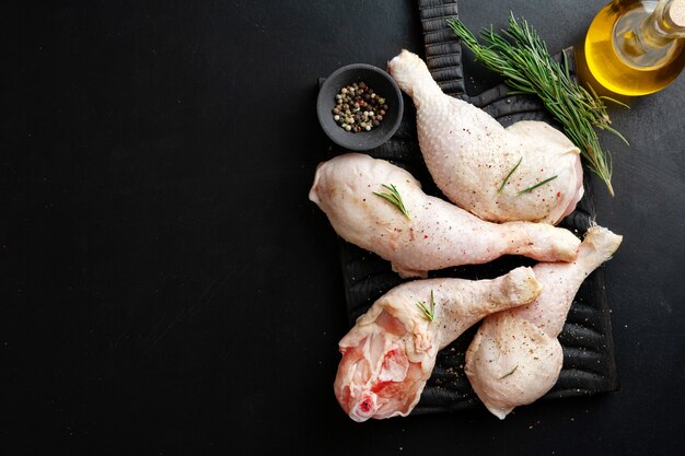 Rohe Hähnchenschenkel mit Gewürzen an Bord auf dunkler Oberfläche