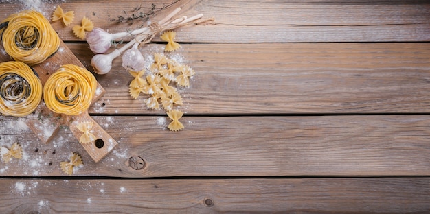 Rohe hausgemachte Pasta mit Mehl, Knoblauch und Gewürzen auf dem rustikalen Hintergrund. Ungekochte Nudeln. Ansicht von oben