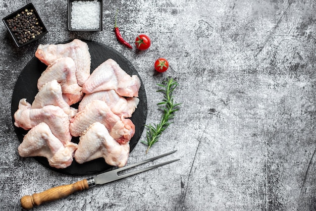 Rohe Hühnerflügel auf einem Teller mit Messer und Gabel auf grauem Hintergrund.