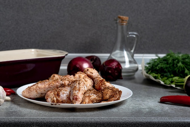 Rohe Hühnerflügel mit Gewürzen auf einem weißen Teller auf dem Küchentisch Vorbereitung zum Grillen