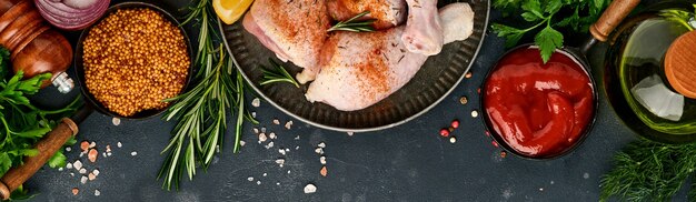 Rohe Hühnerkeulen mit Zutaten zum Kochen auf schwarzem Steinhintergrund. Lebensmittel Hintergrund,