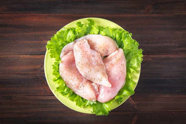 Rohe Hühnerleiste und grüner Salat in einer gelben Schüssel auf dem Hintergrund eines Holztischs.