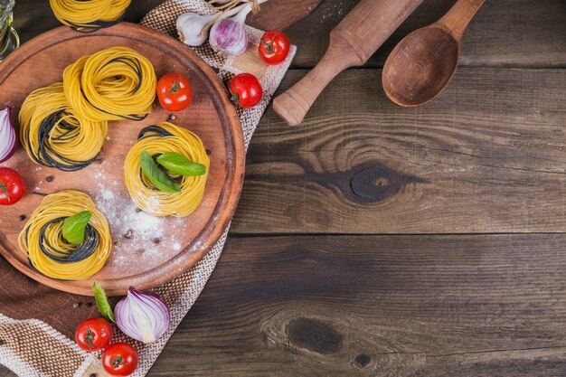 Rohe italienische Pasta mit Zutaten. Kirschtomaten, ungekochte Spaghetti, rote Zwiebeln und Kräuter auf einem dunklen rustikalen Holztisch. Kochkonzept. Draufsicht mit Kopienraum für Text