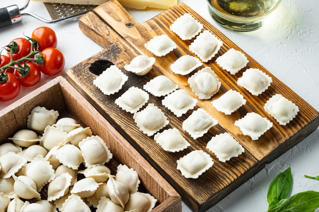 Rohe italienische Ravioli Tortellini mit frischem Parmesan und Basilikum, Tomaten auf Holzbrett, auf weißem Hintergrund