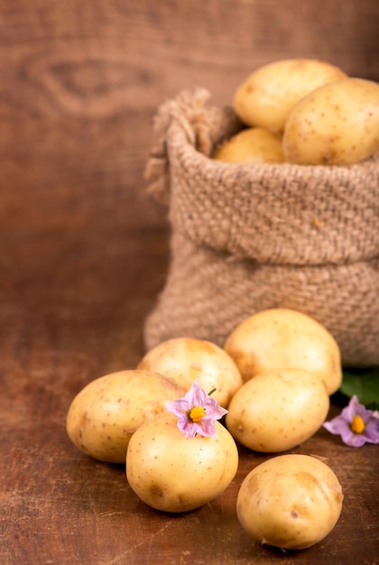 Rohe Kartoffeln mit Blumen in der Tasche auf dem hölzernen Hintergrund