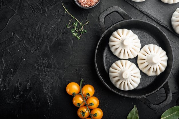 Rohe Knödel Dim Sum Set, in Bratpfanne aus Gusseisen, auf schwarzem Steintisch, Draufsicht flach gelegt