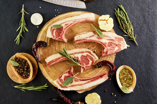 Rohe lammrippen mit zutaten zum kochen: salz, pfeffer, olivenöl und kräuter auf einem holzständer. draufsicht