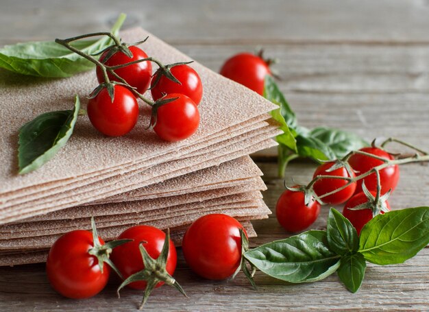 Rohe Lasagneblätter, Basilikum und Kirschtomaten auf einem Holztisch