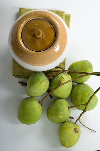 Rohe Mango und traditionelles indisches Gurkenglas, das auf weißem strukturiertem Hintergrund platziert wird, selektiver Fokus und Draufsicht