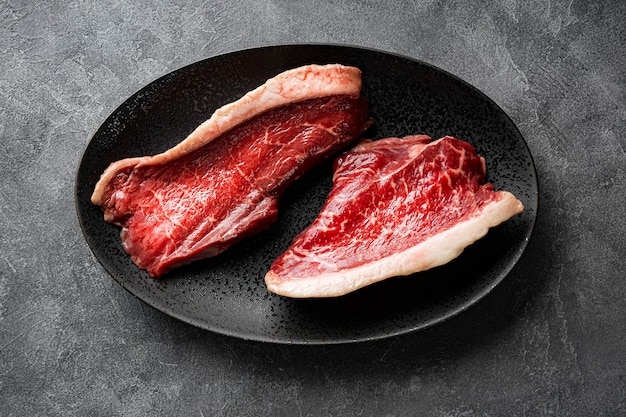 Rohe marmorierte Rindersteaks auf der schwarzen Platte und dunkelgrauem Hintergrund, Ansicht von oben. Rohes Rindfleisch auf dem Küchentisch. Foto in hoher Qualität