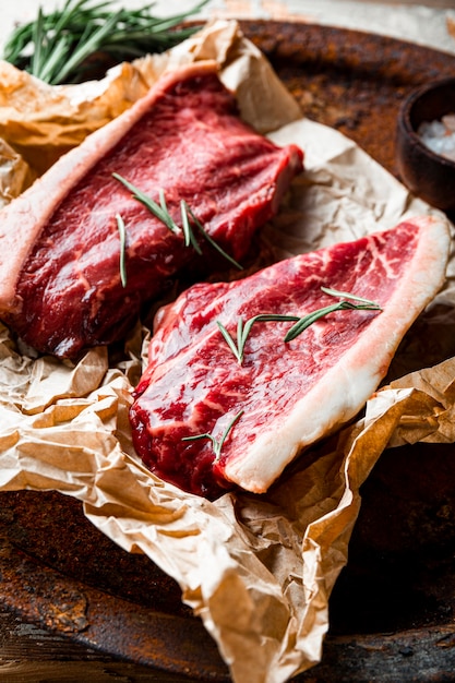 Rohe marmorierte Rindersteaks und Gewürze für ihre Zubereitung auf dem alten Holzhintergrund, vertikales Foto. Rohes Rindfleisch auf dem Küchentisch. Foto in hoher Qualität