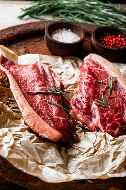 Rohe marmorierte Rindersteaks und Gewürze für ihre Zubereitung auf dem alten Holzhintergrund, vertikales Foto. Rohes Rindfleisch auf dem Küchentisch. Foto in hoher Qualität