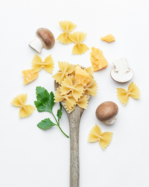 Rohe Nudeln mit Pilzen und Parmesan in einem Holzlöffel auf weißem Hintergrund