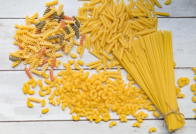 Rohe Nudeln verschiedene Arten von ungekochten Nudeln, Makkaroni, Spaghetti und Nudeln auf hölzernem italienischem Essen kulinarisches Konzept Sammlung verschiedener roher Nudeln auf dem Kochtisch zum Kochen von Speisen