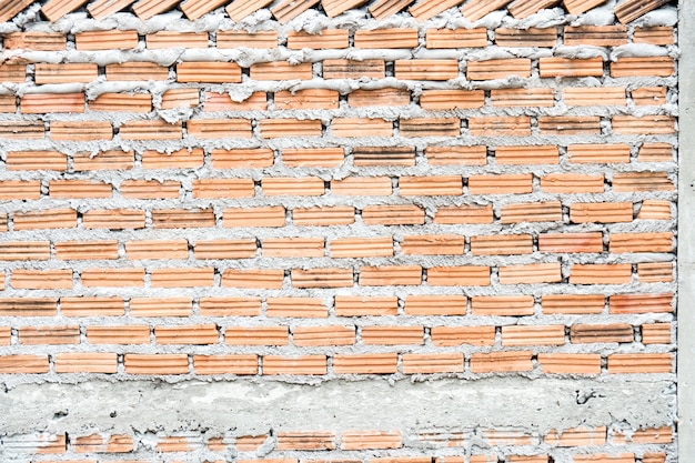 Rohe orange Backsteinmauer vor Zement, Schmutzhintergrundbeschaffenheit