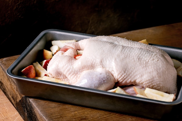 Rohe organische ungekochte junge ganze Ente mit geschnittenen Äpfeln im Backblech, das auf Holztisch steht.