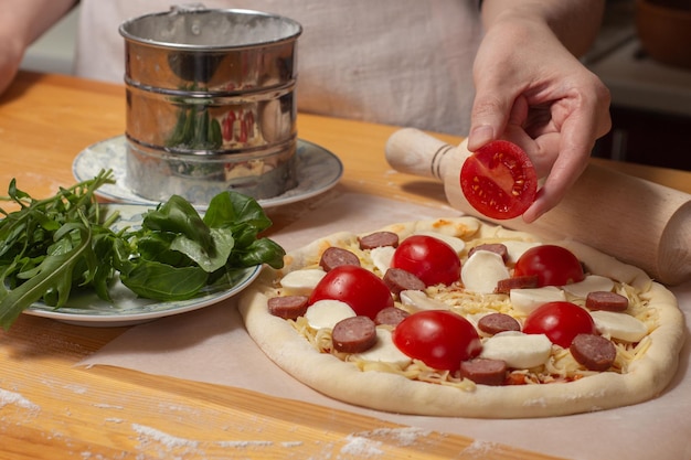 Rohe Pizza auf Bäckerpapier auf dem Holztisch Zubereitung hausgemachter ungekochter Käsepizza mit Tomate