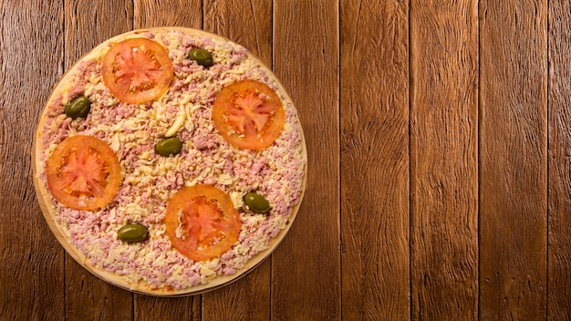 Rohe Pizza mit Käse und Schinken auf Holztisch