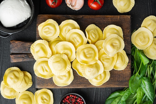 Rohe Ravioli mit Ricotta und Spinat, auf Holzschneidebrett, auf schwarzem Holztisch, Draufsicht flach gelegt