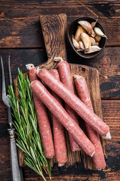 Rohe Rind- und Schweinswurst auf altem Schneidebrett mit Weinlesefleischgabel. Dunkler hölzerner Hintergrund. Draufsicht.