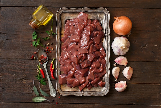 Rohe Rinderleber mit Gewürzen, Kräutern und Gemüse auf einem Holztisch