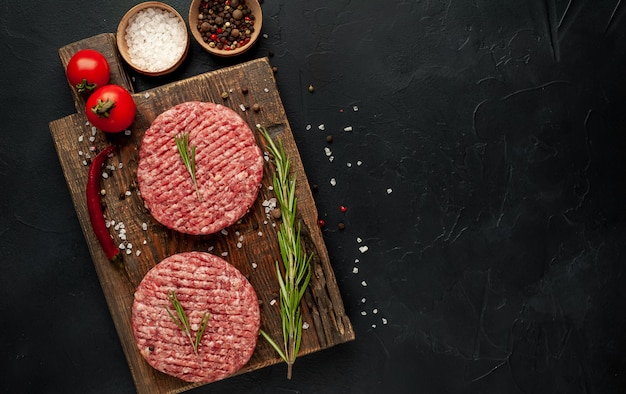 Rohe Rindfleisch-Burger-Schnitzel mit Kräutern und Gewürzen auf einem konkreten Hintergrund mit Kopierraum für Ihren Text