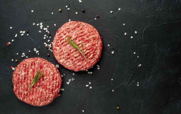 Rohe Rindfleisch-Burger-Schnitzel mit Kräutern und Gewürzen auf einem konkreten Hintergrund mit Kopierraum für Ihren Text