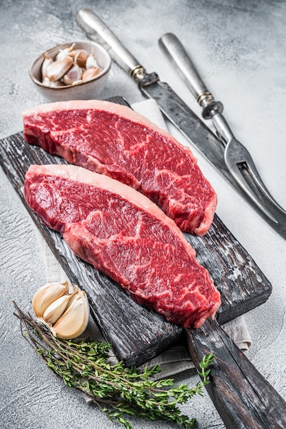 Rohe Rump-Rindfleisch-Steaks auf Holzbrett mit Fleischmesser und Gabel. Weißer Hintergrund. Ansicht von oben.