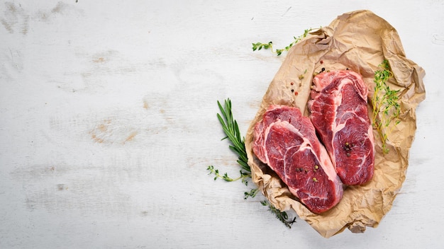 Rohe saftige Ribeye-Steaks mit Gewürzen auf einem weißen Holztisch Draufsicht Freier Platz für Ihren Text