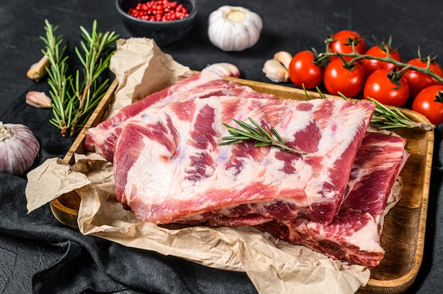 Rohe Schweinefleischrippen mit Bestandteilen für das Kochen des Rosmarins und des Knoblauchs in einer hölzernen Schüssel. Ansicht von oben