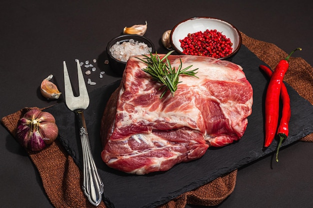 Rohe Schweinelende mit Gewürzen und Kräutern, frisches Fleisch, geschnittene Zutat zum Kochen von proteinhaltigen Lebensmitteln, gesunde Ernährung, trendiger, harter, heller, dunkler Schatten, schwarzer Steinbetonhintergrund in Nahaufnahme