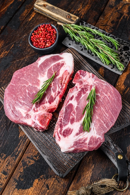 Rohe Schweinelendensteaks mit Kräutern auf einem Schneidebrett mit Fleischerbeil