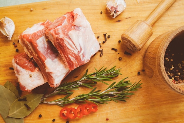 Rohe Schweinerippenkoteletts auf geschnittenem Brett mit Rosmarin-Pfeffer-Knoblauch und Lorbeerblatt-Vintage-Fotoverarbeitung