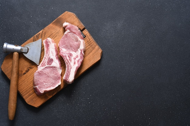 Rohe Schweinesteaks auf einem Brett mit einer Axt auf dunklem Hintergrund. Sicht von oben. Frischfleisch. Rippen.