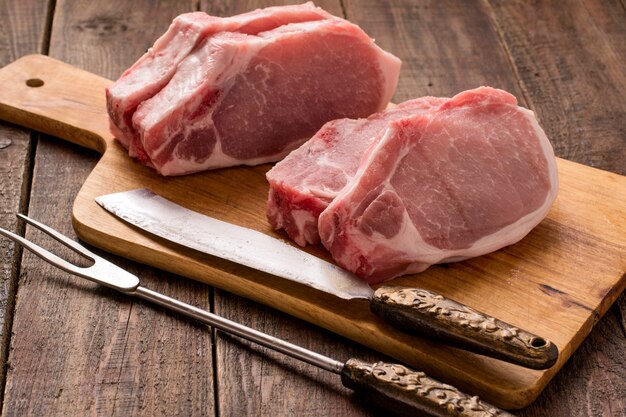 Rohe Schweinesteaks auf Schneidebrettmesser und Gabel zum Schneiden von Fleisch