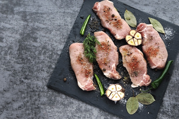 Rohe Schweinesteaks mit Gewürzen vor dem Kochen. Appetitliches Fleisch auf einem Steinbrett mit Gewürzen.