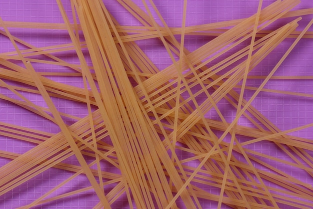 Rohe Spaghetti auf lila Hintergrund Vegetarisches Essen-Konzept Nahaufnahme einer italienischen Pasta Ansicht von oben